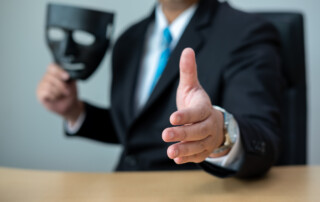 A business man with a black mask covering the insincerity of doing business together.Corruption concept.